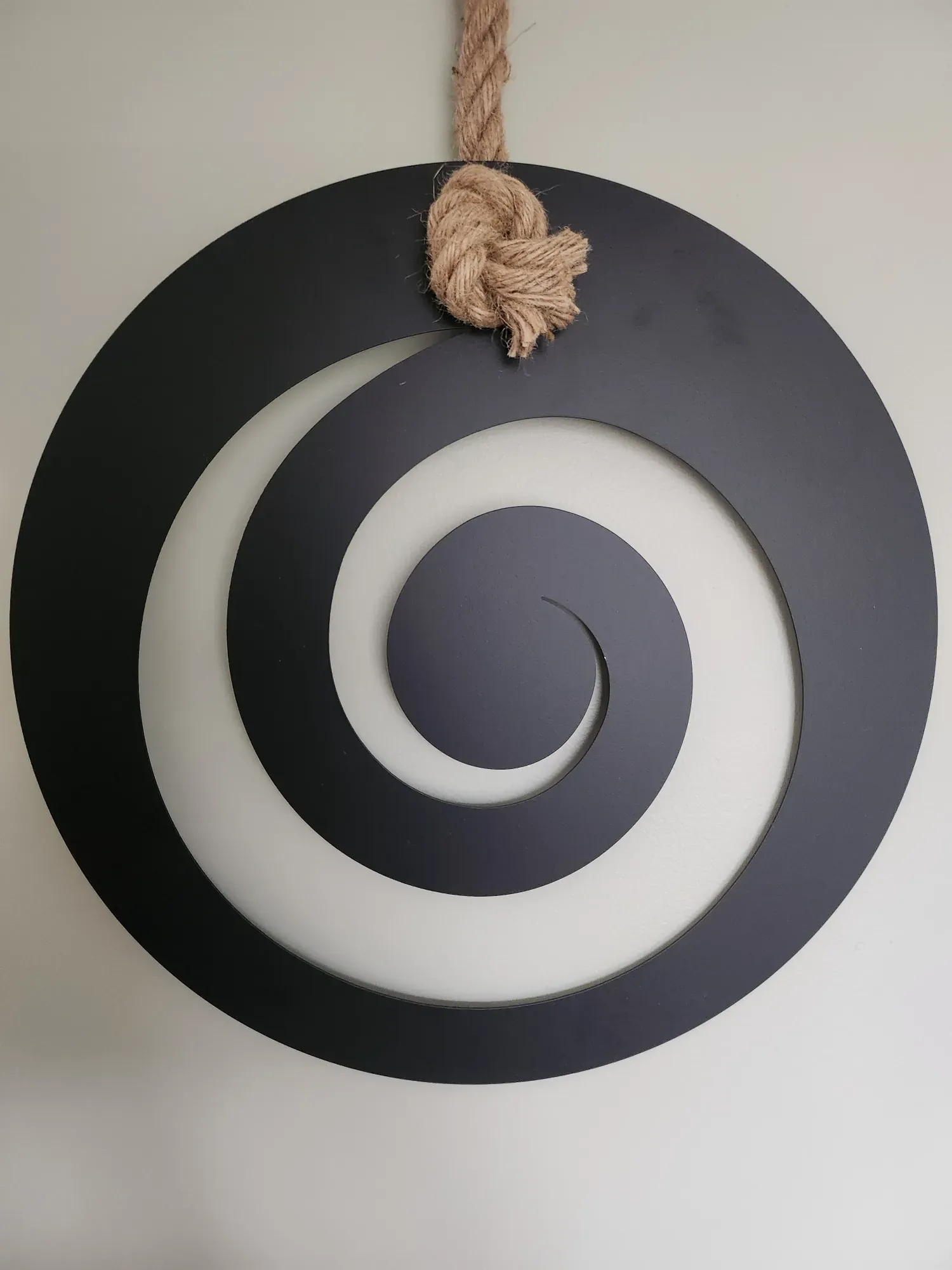 A large black koru spiral, cut from a single disc, hanging on the wall of the session room from a knotted rope.